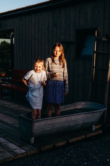 Zlaté světlo letního večera na tvářích dětí, které si chladí nohy v kovové vaně na terase tiny housu.