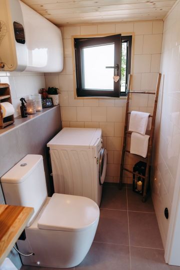Pohled na wc a pračku v designové koupelně s dřevěnými detaily v tiny housu v glampingu nádech.