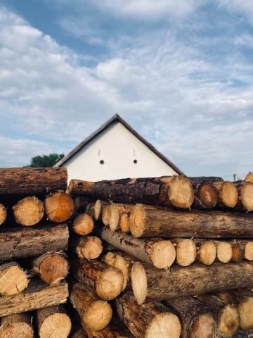 Detailní záběr na naskládaná polena dřeva s bílým domem a modrou oblohou v pozadí na statku nádech.