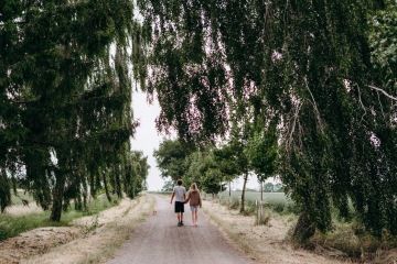 Pár se psem procházející se po cestě obklopené zelenými stromy v okolí statku nádech na Vysočině.