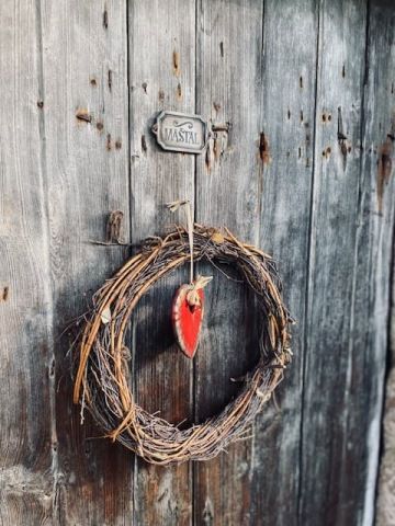 Ručně dělaný dřevěný věnec s červeným srdcem uprostřed zavěšený na starých dřevěných dveřích s cedulkou "MAŠTAL" na statku nádech.